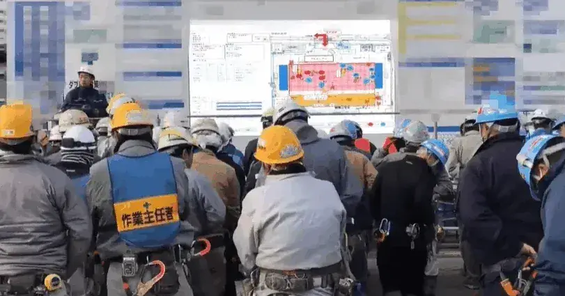 朝礼で大型ビジョンに図面を映し、作業内容を説明している様子
