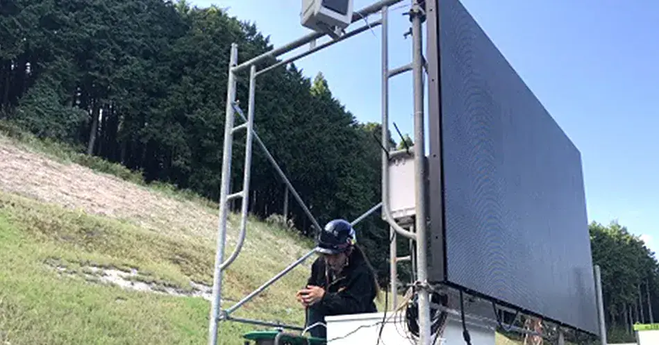 法面の現場に設置したLEDビジョンと、映像を操作する作業員