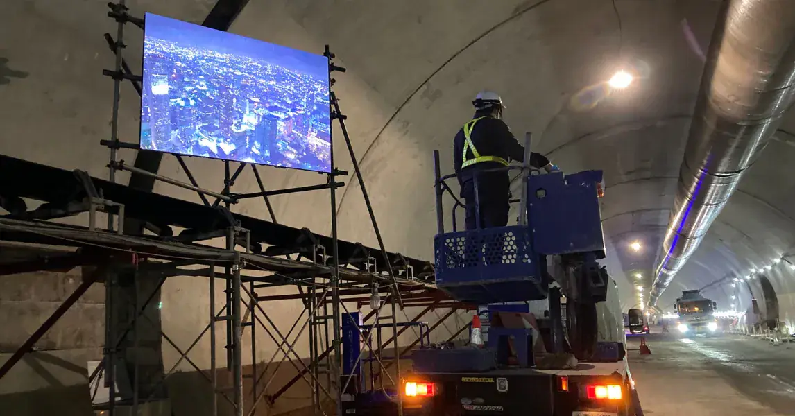 トンネル工事の坑内に設置したLEDビジョンと、高所作業車で作業する作業員